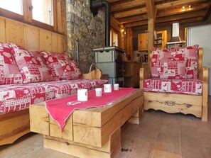 L’intérieur d’un chalet accueillant, avec un canapé et un fauteuil en bois, une table en bois et un mur en pierre.