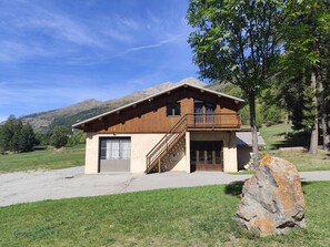 Eine zweistöckige Holzhütte mit Balkon, Garage und einem großen Felsen im Vordergrund.