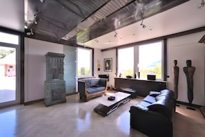 Amplia sala de estar con techo alto, ventanas grandes, chimenea y mobiliario moderno.