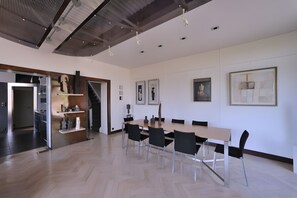 Een moderne eetruimte met een houten tafel, zwarte stoelen, een trap en kunstwerken aan de muren.