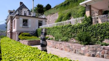 A two-story house with a stone retaining wall and a white fence.