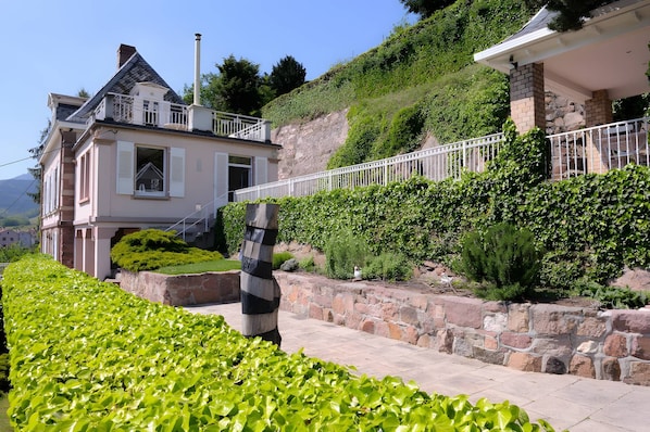 A two-story house with a stone retaining wall and a white fence.