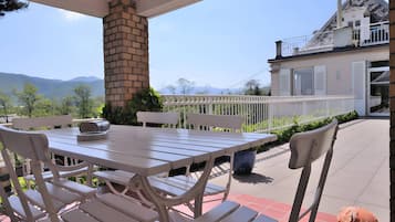 Une terrasse extérieure avec une table et des chaises, une cheminée en briques et une vue sur une maison dotée d’un balcon.