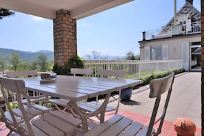 Een terras buiten met een tafel, stoelen, een bakstenen schoorsteen en uitzicht op een huis met een balkon.