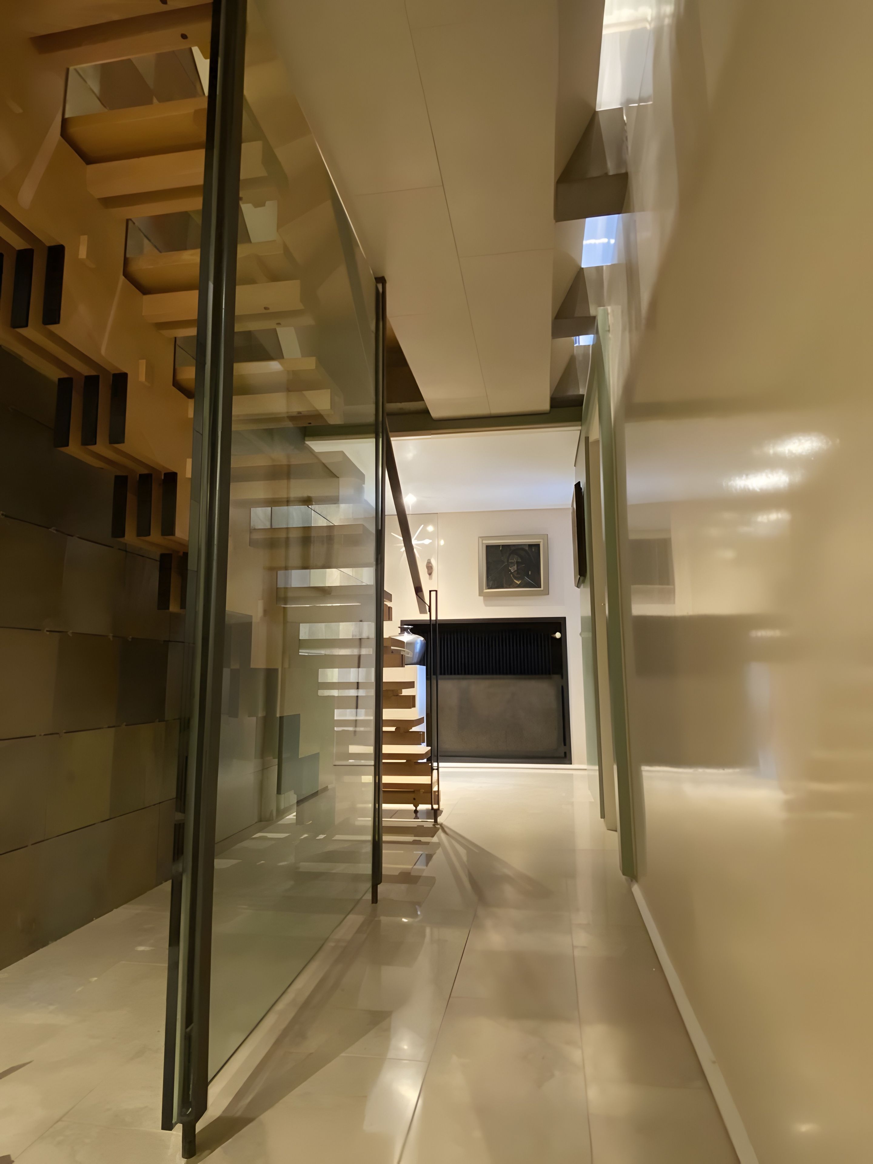 Un interior moderno con una escalera de cristal que lleva a un espacio de tonos oscuros.