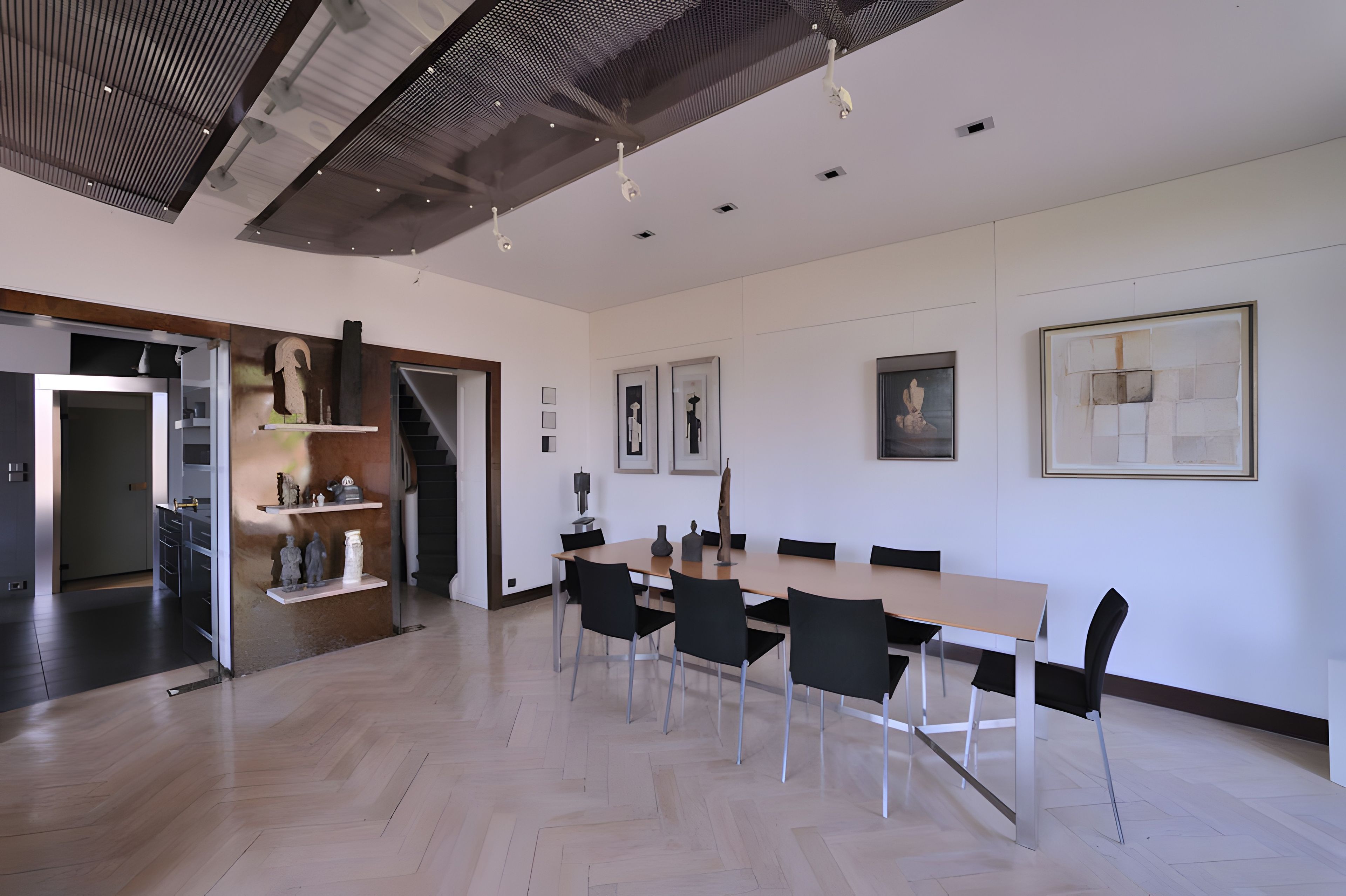 Un comedor moderno con una mesa de madera y sillas negras, una escalera y obras de arte en las paredes.