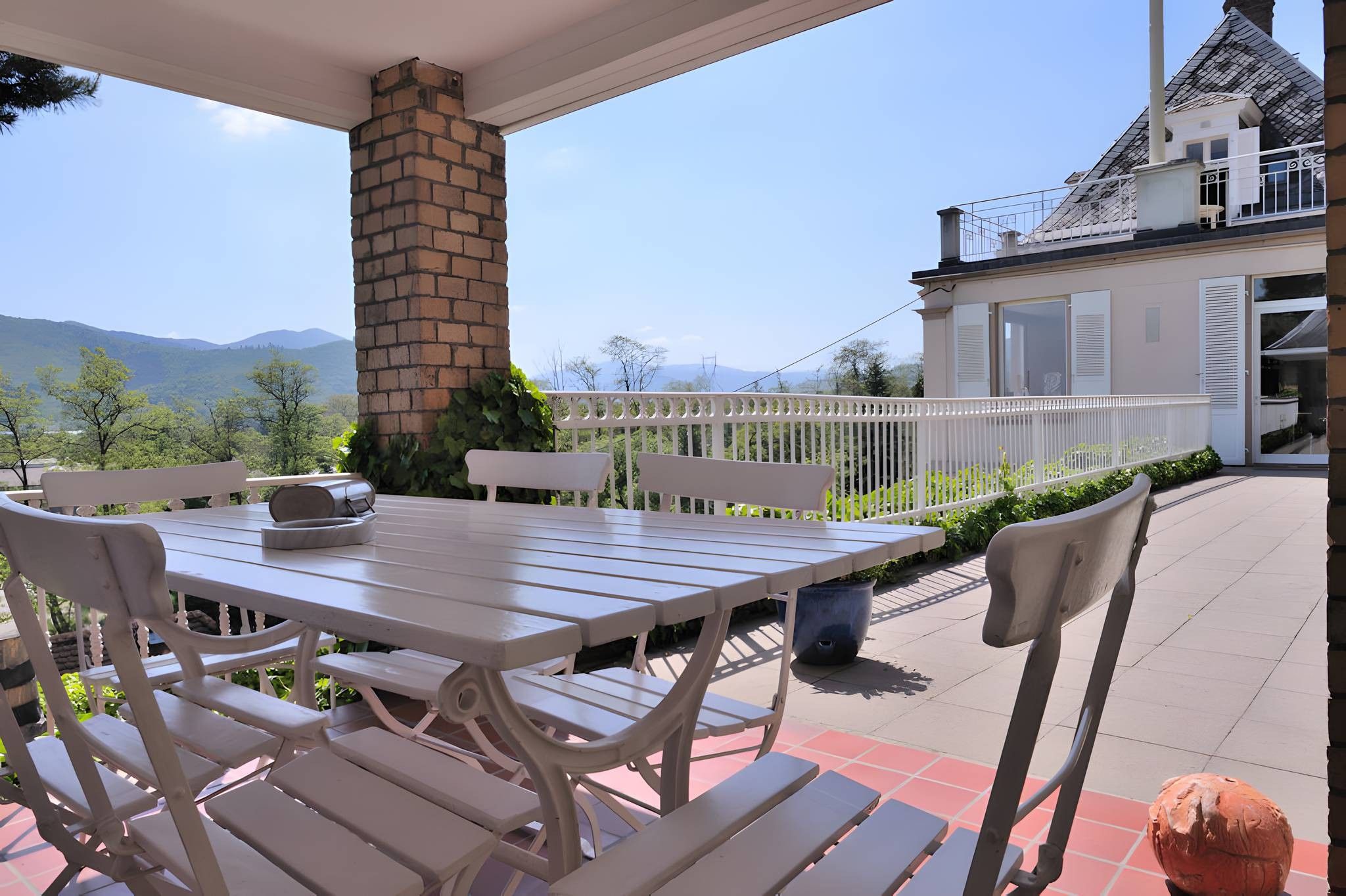 Un patio exterior con mesa y sillas, una chimenea de ladrillo y vista a una casa con balcón.
