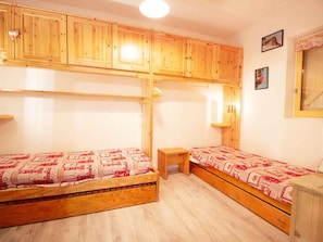 A room with two wooden beds, a small wooden table, and a mirror on the wall. - Calm apartment near the forest - 4 guests (Villarodin-Bourget)