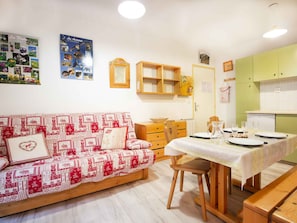 A cozy room with a sofa, a dining table set for two, wooden cabinets, and a wall decorated with framed pictures. - Calm apartment near the forest - 4 guests (Villarodin-Bourget)