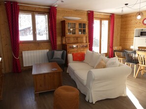 A cozy room with a white sofa, a wooden cabinet, a dining table with chairs, and red curtains. - Quiet chalet - 6 guests (Pralognan-la-Vanoise)