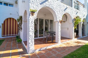 A building with white stucco walls, red and yellow striped doors, and a patio area with a table and chairs. - Apartment in Nerja Near El Playazo Beach (Nerja)
