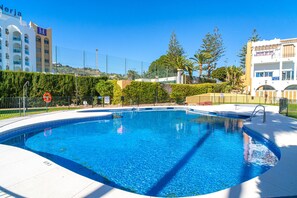 A swimming pool with a clear blue water, surrounded by a white deck, and a fence. - Apartment in Nerja Near El Playazo Beach (Nerja)