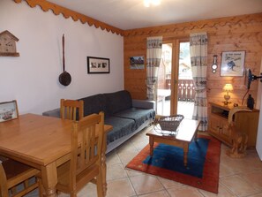 A cozy living room with a wooden table, a sofa, a wicker chair, and a small table with a lamp. - Charming apartment near center - 4 guests (Pralognan-la-Vanoise)