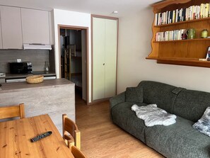 Kompakti oleskelutila, jossa on pieni keittiönurkkaus, sohva, kirjahylly ja ruokailualue.