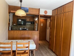 A compact kitchen with wooden cabinets, a microwave, and a small dining area with a table and chairs. - Studio cabin, pets welcome - 4 guests (Pralognan-la-Vanoise)