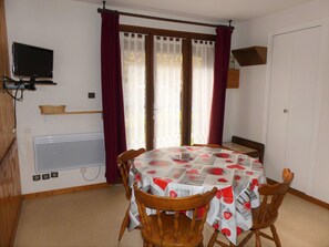 A dining area with a round table, four wooden chairs, a television mounted on the wall, and a window with curtains. - Well-located studio cabin, cats OK - 4 guests (Pralognan-la-Vanoise)