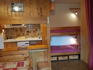 Ein kompaktes Zimmer mit Küchenzeile, Etagenbetten und einem kleinen Tisch.
