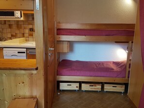 Ein kompaktes Zimmer mit Etagenbett, einer Küchenzeile inklusive Geschirrspüler von Bosch und einem Holzkasten.