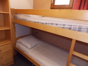 Een stapelbed met een onderbed en een enkel bed. Links staat een houten plank met lades.