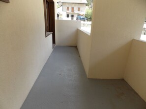 Ein enger Gang mit einem Balkon, der zu einem Gebäude führt, an dem ein Fenster sichtbar ist und sich ein Auto davor geparkt befindet.
