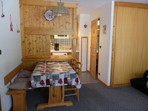 Ein Essbereich mit Holztisch und Bänken, eine Küche im Hintergrund und eine Tür zu einem anderen Raum.