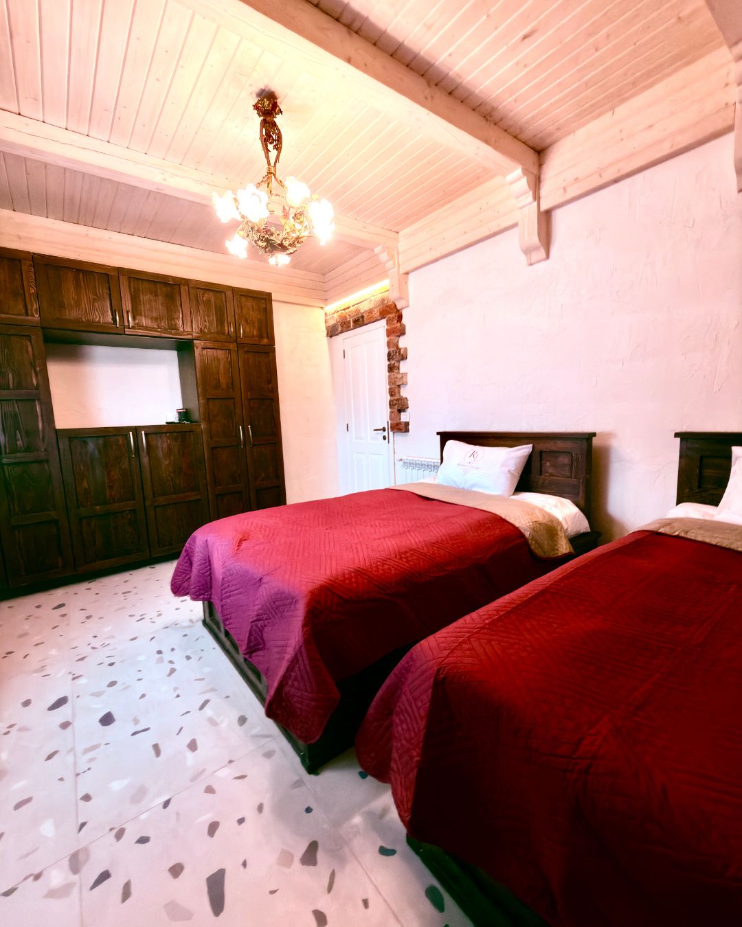 Ein Zimmer mit zwei Betten, Holzschränken, einer Chandelieber und einer weißen Tür.