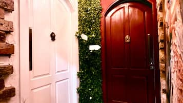 A hallway with a white door, a red door, and a green wall with foliage.