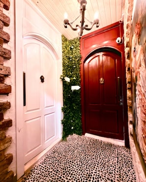 A hallway with a white door, a red door, and a green wall with foliage.