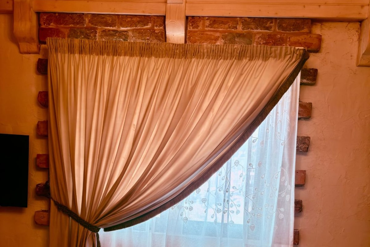 A room with a bed, a window with sheer curtains, and a brick wall.