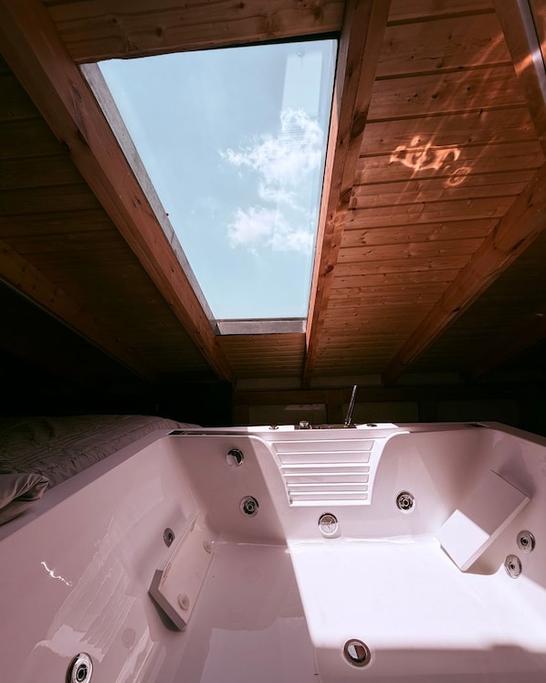 Un bain à remous avec une lucarne au-dessus, des poutres en bois et un lit.