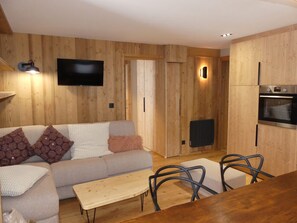 A modern living room with a sofa, a coffee table, and a TV mounted on the wall. - Modern apartment with terrace - 6 guests (Pralognan-la-Vanoise)