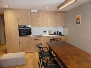 Eine moderne Küche mit Holzschränken, einem eingebauten Ofen, einer Marmor-Spritzschutzleiste und einem Essbereich mit Holztisch und -stühlen.