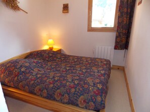 A single bed with a floral-patterned bedspread in a room with a window, a radiator, and a lamp on a bedside table. - Ideal apartment with balcony - 4 guests (Pralognan-la-Vanoise)