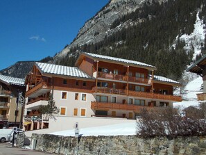 A multi-story hotel with balconies, a stone wall in front, and a mountainous backdrop. - Ideal apartment with balcony - 4 guests (Pralognan-la-Vanoise)