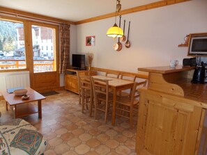A wooden interior with a dining table, chairs, a television, and a kitchen area. - Ideal apartment with balcony - 4 guests (Pralognan-la-Vanoise)