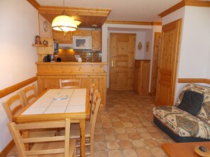 Una cucina funzionale con mobili in legno, un tavolo da pranzo e sedie. Si nota un forno a microonde e un lavandino. Sullo sfondo, un divano.