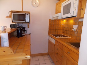 Una cucina compatta con mobili in legno, un forno a microonde, una macchina da caffè e un lavello.