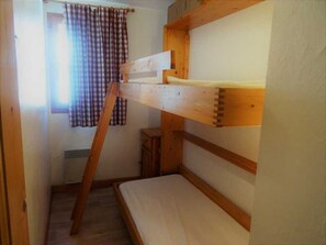 A bunk bed with a wooden frame, a small wooden stool, and a window with curtains. - 2-room apartment - 6 guests - Pralognan (Pralognan-la-Vanoise)
