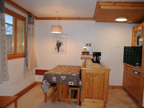 A kitchen with wooden cabinets, a table with a patterned tablecloth, and a poster on the wall. - 2-room apartment - 6 guests - Pralognan (Pralognan-la-Vanoise)