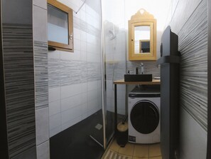 Een kleine badkamer met een douchecabine van glas, een wastafel, een spiegel en een wasmachine.