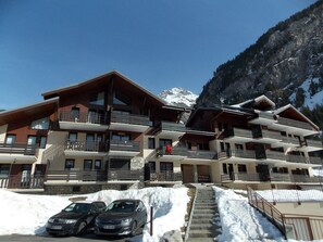 A multi-story hotel with balconies, a staircase leading to the entrance, and a snowy mountain backdrop. - Apartment with stunning view - 6 guests (Pralognan-la-Vanoise)