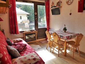 A cozy living room with a red patterned sofa, wooden dining table with chairs, and a fireplace. - Renovated studio, mountain view - 4 guests (Pralognan-la-Vanoise)