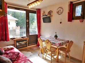 A cozy room with a sofa, a table with chairs, a fireplace, and a window with curtains. - Renovated studio, mountain view - 4 guests (Pralognan-la-Vanoise)