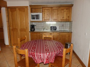 A kitchen with wooden cabinets, a microwave, a coffee maker, and a table with a patterned tablecloth. - Cozy and sunny apartment - 4 guests (Pralognan-la-Vanoise)