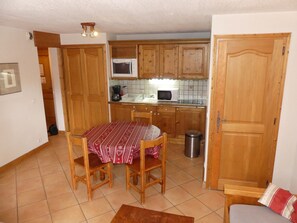A compact kitchen with wooden cabinets, a microwave, and a dining table with chairs. - Cozy and sunny apartment - 4 guests (Pralognan-la-Vanoise)