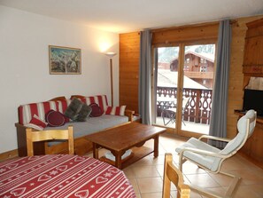 Ein gemütliches Zimmer mit einer Couch, einem Holztisch, einem Stuhl und einer Glastür zu einem Außenbereich.