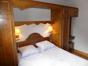 A wooden-framed bed with two white pillows and a quilted blanket, flanked by two wall-mounted lamps. - Cozy and sunny apartment - 4 guests (Pralognan-la-Vanoise)