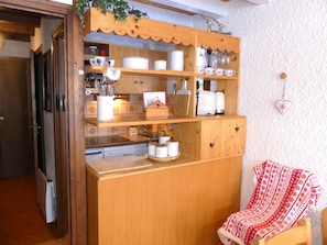 A kitchen with wooden cabinets, a sink, and a chair with a patterned blanket. - Duplex in Pralognan - 4 guests (Pralognan-la-Vanoise)