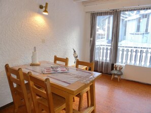 A dining area with a wooden table, chairs, a decorative lamp, and a window with a view. - Duplex in Pralognan - 4 guests (Pralognan-la-Vanoise)