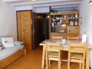 A cozy room with a wooden dining table, chairs, a sofa with a heart-shaped pillow, and a kitchen area with wooden cabinets and shelves. - Duplex in Pralognan - 4 guests (Pralognan-la-Vanoise)
